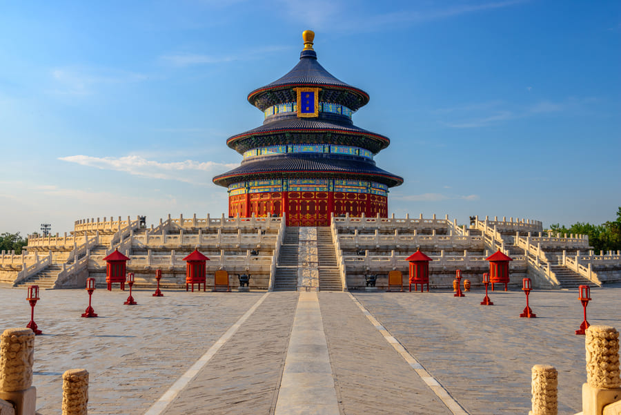 El Templo del Cielo en Beijing con su característica sala circular de tejado azul, bajo un cielo despejado. El pabellón está enmarcado por escaleras de piedra y lámparas rojas tradicionales.