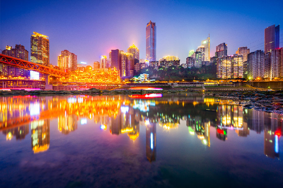 Horizonte nocturno de Chongqing con rascacielos iluminados, el complejo Hongyadong y el puente Dongshuimen reflejados en el agua, China.