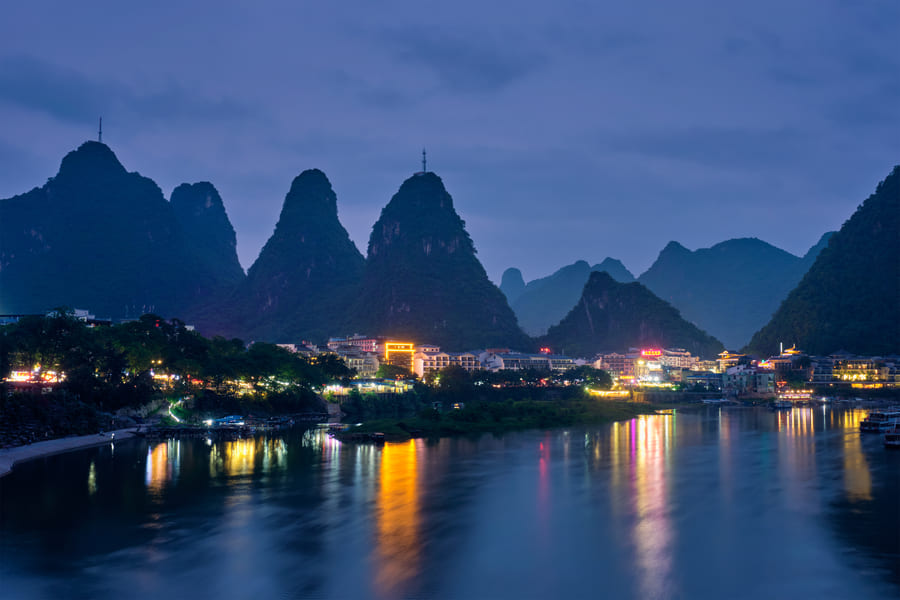 Vista nocturna de la ciudad de Yangshuo en Guilin, China, con las luces urbanas reflejadas en el río Li frente a montañas kársticas.